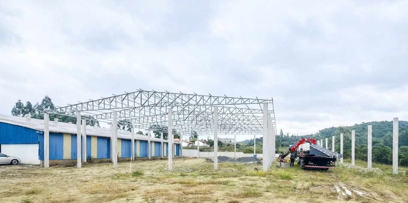 Estrutura metálica de galpão agrícola em montagem ao lado de barracão existente