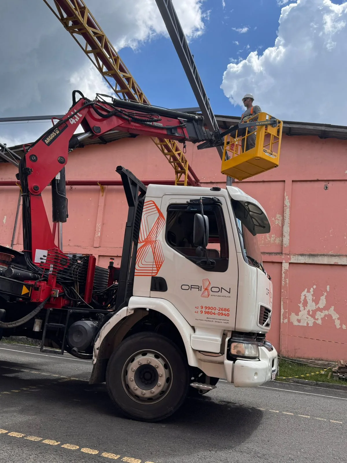 Caminhão-guindaste da Orion em obra com operário sobre cesta aérea